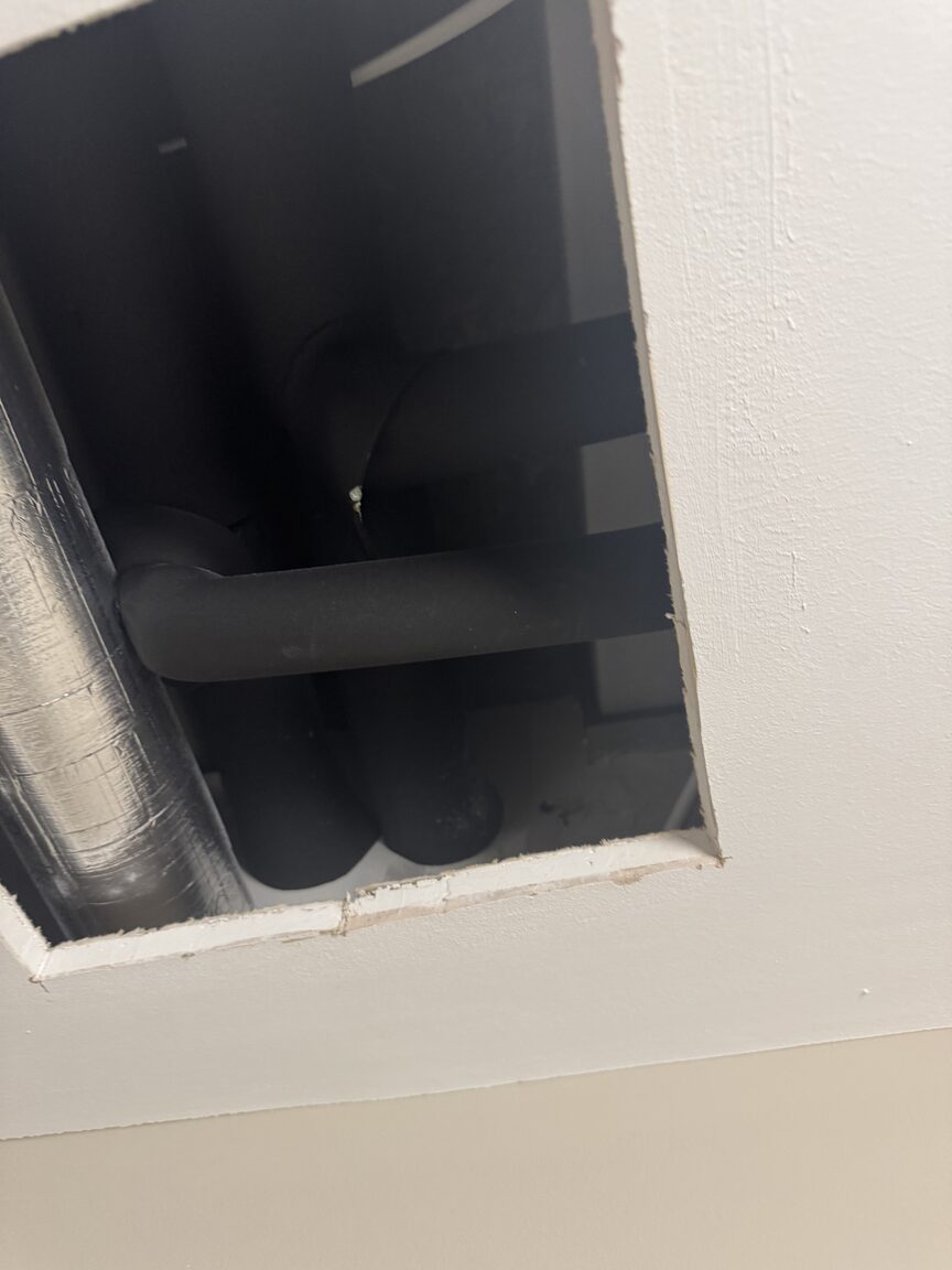 Opened ceiling access hatch showing insulated pipework running through the void