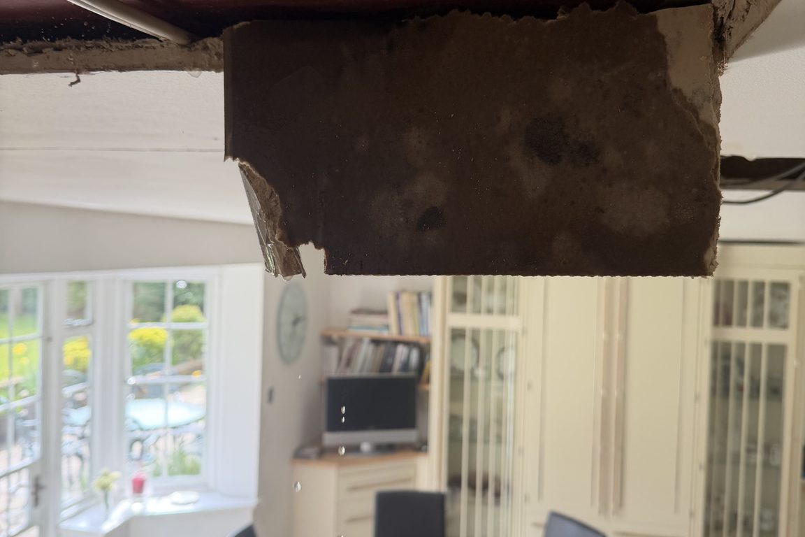 Water-stained plasterboard hanging from an opened kitchen ceiling beneath a steel beam
