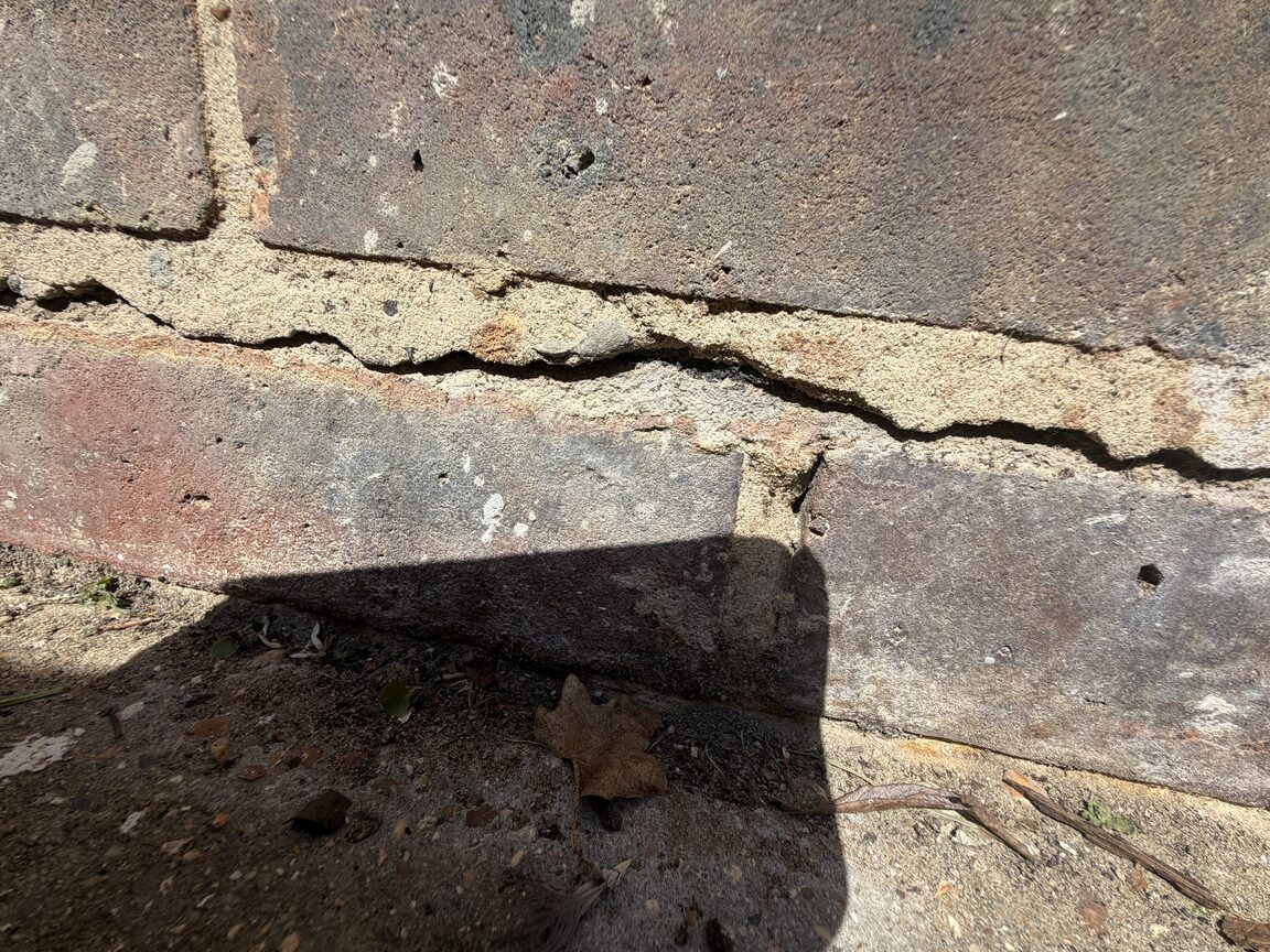 Cracked mortar joint running along an external brick plinth near ground level