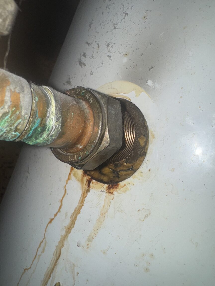 Corroded compression fitting leaking on a hot water cylinder, with rust staining running down below it