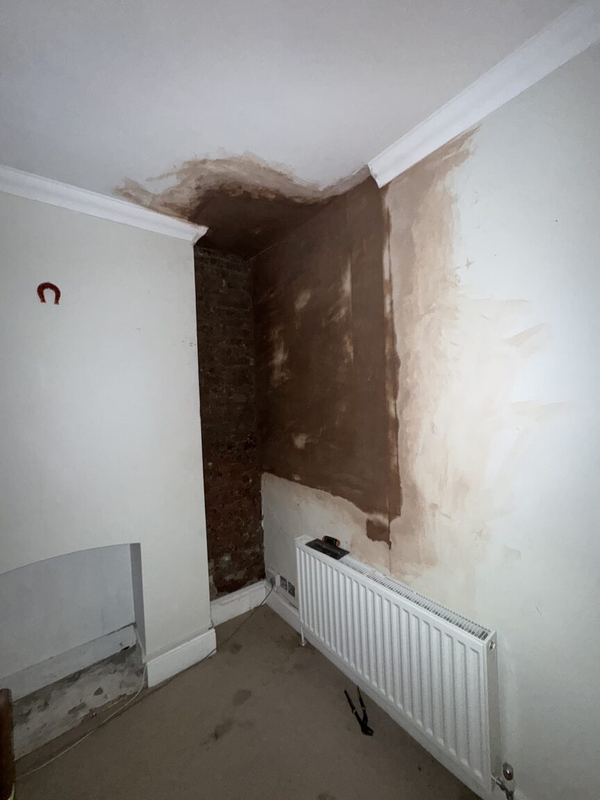 Room corner stripped back to bare brick and freshly re-plastered after damp treatment, radiator alongside