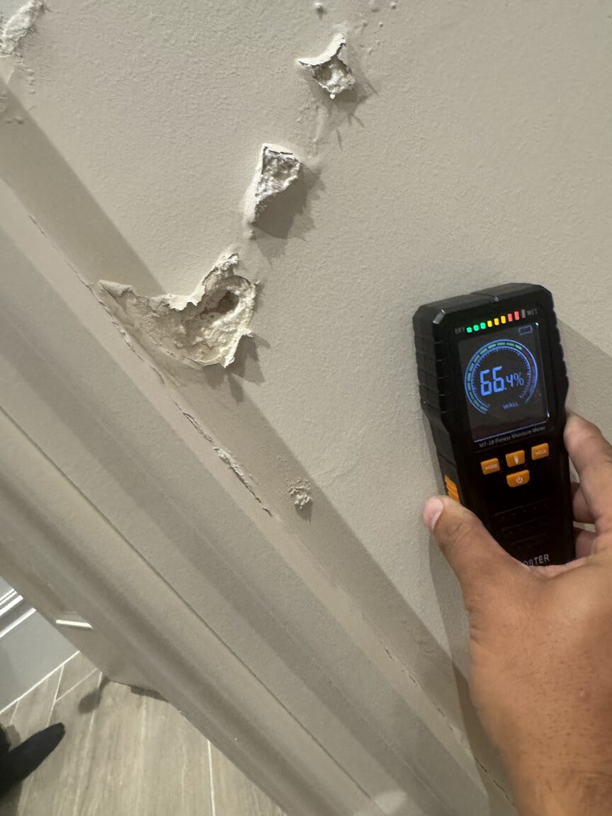 Pinless moisture meter reading 66 per cent held against a damaged wall at ceiling height