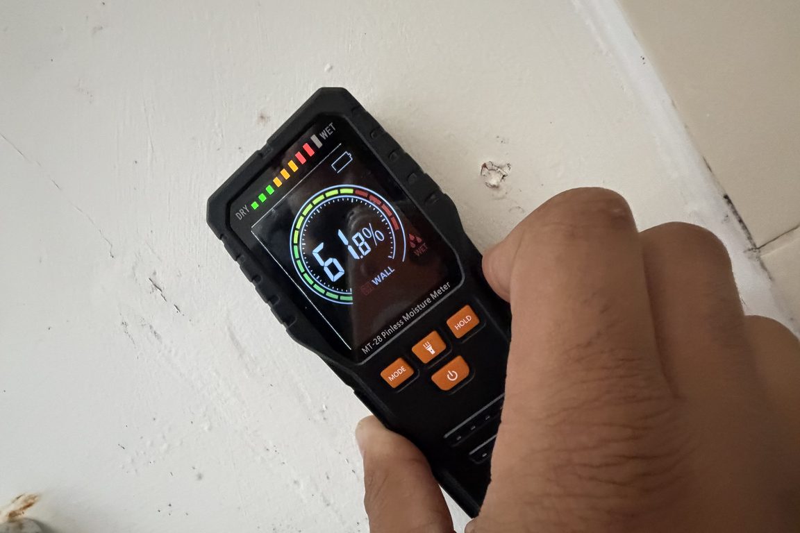 Hand-held moisture meter reading 61.8 percent in the wet range on a ceiling