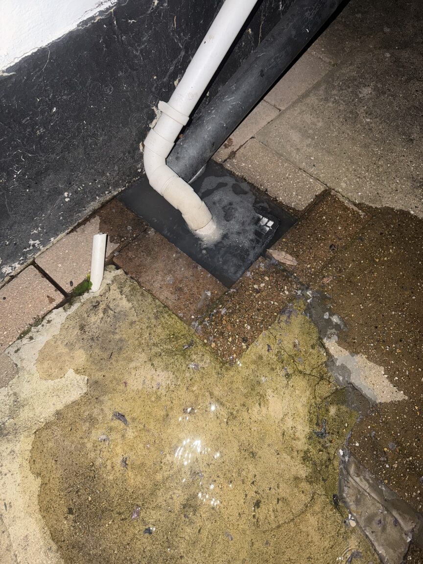 Downpipe discharging into a flooded, blocked external gully at night