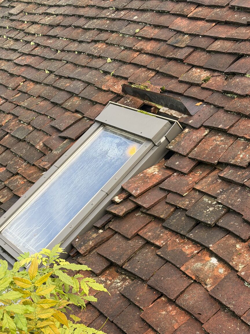 Roof window surrounded by slipped and broken roof tiles
